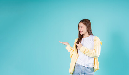 Happy young Asian woman pointing at open hand with a smile against a blue background, perfect for...