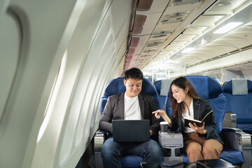 A young Asian businessman and woman are talking and looking at information on their laptops and...