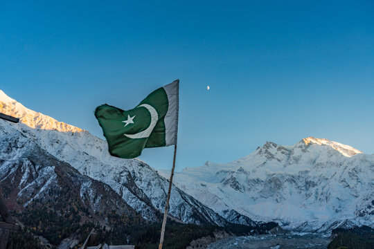 Pakistani national flag waving at the famous Fairy Meadows camping site with the Nanga Parbat mountain (8,126m) illuminated by golden sunrise light in the background in Gilgit-Baltistan region