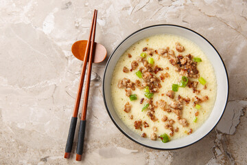 Delicate soft steamed eggs with crispy fried pork mince and green onions close-up in a bowl on the table. Horizontal top view from above
