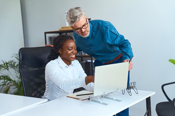Collaborative office interaction between a senior male mentor and a young female professional,...