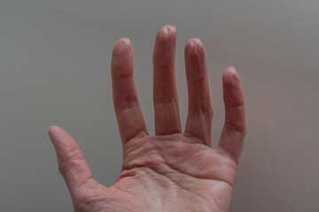 Outstretched human hand with visible skin texture and wrinkles, positioned against a neutral gray...