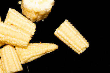 Close up of baby sweetcorn chopped on black background