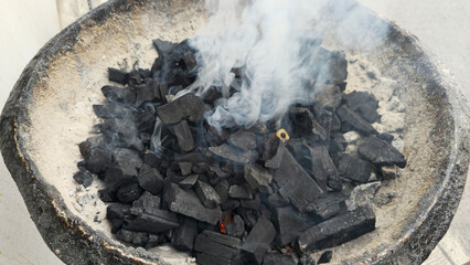 Charcoal for cooking. Smoke rises from the burning charcoal in the stove. Smoke from charcoal on burning charcoal. Preparing the fire for cooking. Close-up of a pile of firewood.