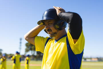 Male baseball player adjusting batting helmet on diamond, wearing jersey and compression sleeve