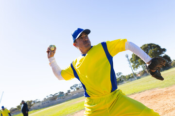 Male baseball player pitching baseball on mound at baseball field in yellow-blue uniform with glove