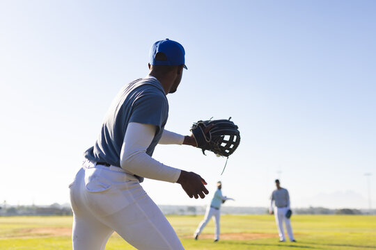 Diverse male baseball players fielding ground ball on grassy baseball field with caps and gloves