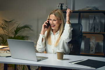 Businesswoman Celebrating Success While Talking On Phone, Sitting At Desk With Laptop And Coffee...