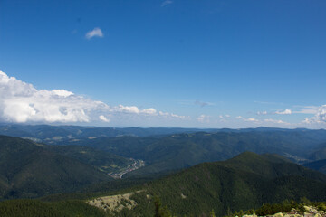 Panoramic view of endless forested mountain ridges and valleys under bright blue sky with white...
