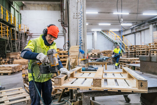 Carpenter assembling wooden pallets using a nail gun in a recycling factory, promoting sustainability and resource optimization