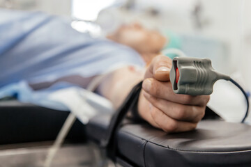Fototapeta premium Patient lying on examination table in medical facility, with hand holding pulse oximeter, showcasing healthcare technology and patient monitoring in clinical environment