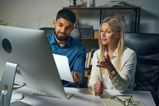 Two Colleagues Collaborating At A Desk, Reviewing Documents And Discussing Work In A Modern Office. The Scene Reflects Teamwork, Productivity, And Professional Interaction.