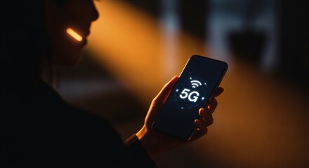 Close-up of a person holding a smartphone displaying a 5G wireless signal at night.