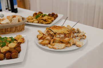 A savory assortment of appetizers including bread, mini pies, croquettes, and cheese dip is served on a buffet table during an indoor event or reception, ready for guests to enjoy.