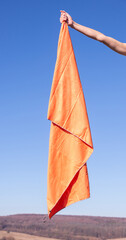 Human hand holding an orange microfiber hiking towel against a clear sky background. Bright outdoor gear for travel, hygiene, and post-shower relaxation
