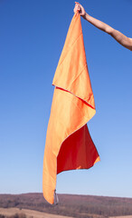 Human hand holding an orange microfiber hiking towel against a clear sky background. Bright outdoor gear for travel, hygiene, and post-shower relaxation