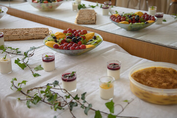Assorted homemade desserts and fresh fruit are beautifully arranged on a white tablecloth during a festive indoor gathering, likely a celebration or family event, in a decorated dining area.