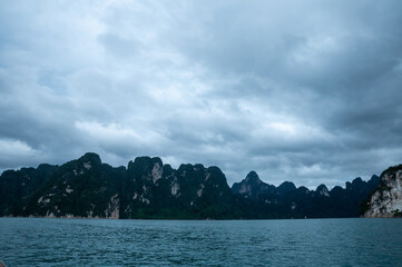 Limestone mountains line the shores of a tranquil lake under a dark sky in southern Thailand.