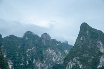 Limestone mountains in southern Thailand are covered with lush greenery, towering under a dark sky....