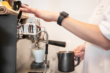 Barista steaming milk with a frothing pitcher at a modern espresso machine, preparing coffee in a...