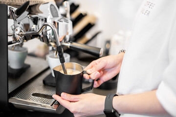 Barista steaming milk with espresso machine steam wand, highlighting milk frothing process, stainless pitcher, and professional coffee preparation in cafe setting.