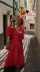 A woman in a bright dress broadcasts live from the streets of Lisbon during the celebration of San...