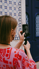 A woman in a bright dress takes a photo of the streets of Lisbon on her mobile phone. Soft focus ....
