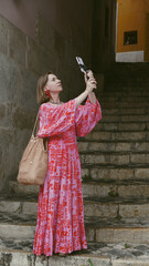 A woman in a bright dress takes a photo of the streets of Lisbon on her mobile phone. Soft focus.