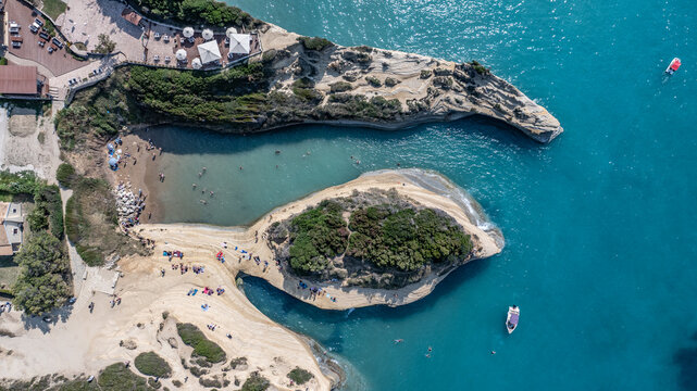aerial top view of area around "Kanali tou Erota" (Channel of Love) beach with people sunbathing and swimming in the bay surrounded by sandstone cliffs - located on north part of Corfu Island