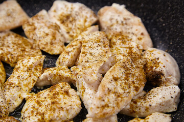 Raw chicken pieces seasoned with spices are sizzling in a frying pan, showcasing the cooking process and vibrant textures of the meat in a culinary setting
