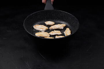 Cooking fish fillets in a frying pan over a dark surface, showcasing the sizzling process and...