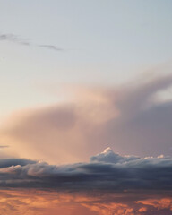 Soft pastel clouds illuminated by sunset light create a serene atmosphere in the sky, showcasing the beauty of nature and the transition from day to night