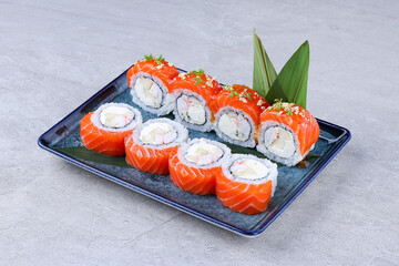 Salmon sushi rolls with shrimp, cream cheese, and fruit filling, garnished with microgreens and crunchy toppings on a blue plate.