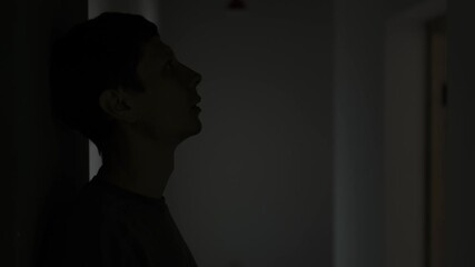 Young man alone after breakup standing in dark corridor feeling deep sadness