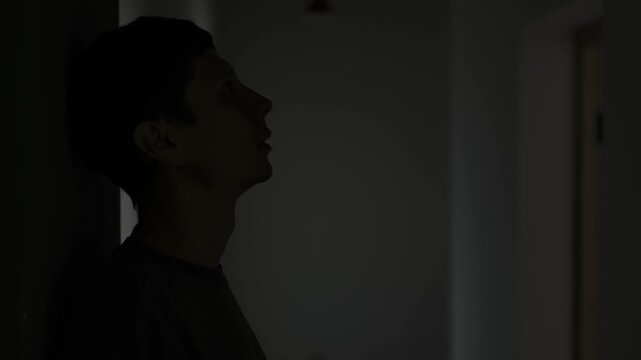 Young man alone after breakup standing in dark corridor feeling deep sadness