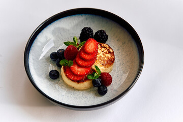 A Beautifully Presented Dessert Featuring Fluffy Pancakes Topped with Fresh Berries and Mint Leaves in a Stylish Bowl
