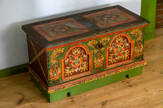 Colorful hand-painted wooden dowry chest decorated with traditional floral folk motifs, placed on a wooden floor in a rustic village interior. Ornate vintage furniture with cultural heritage.