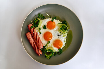 A Delicious Plate of Three Fried Eggs Garnished with Fresh Herbs and Accompanied by Sliced Sausages with Fresh Zucchini Spirals