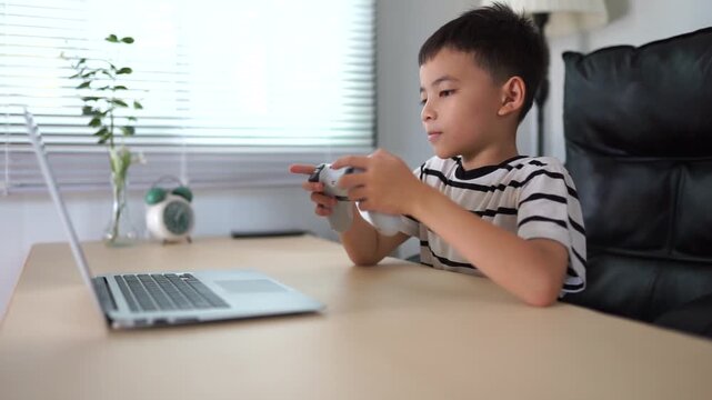 Little boy playing video game on laptop at home sitting at desk