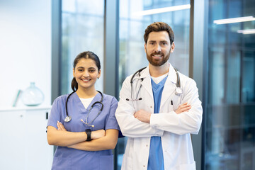 Two healthcare professionals, a doctor and a nurse, stand side by side, smiling confidently, with arms crossed, in a modern medical setting.