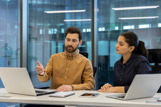 A businessman gestures while explaining something to a businesswoman at a modern office.