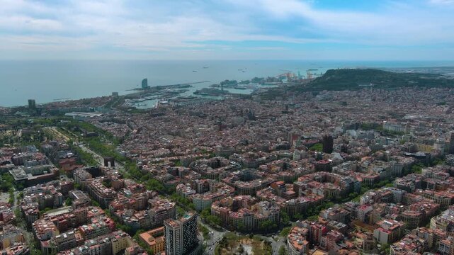 Expansive aerial drone flight over Barcelona's urban cityscape. Revealing the dense architecture, famous skyline, and Mediterranean coast on a beautiful day in Spain.