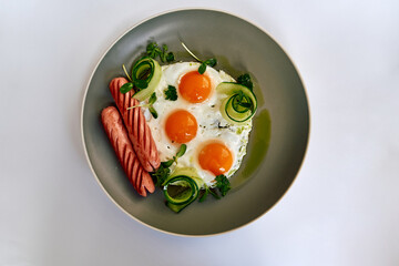 A Flavorful Breakfast Plate Featuring Sunny-Side-Up Eggs, Sliced Sausage, and Fresh Vegetables on a Stylish Gray Plate