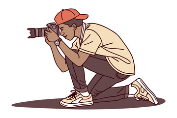 Young man wearing an orange baseball cap and casual clothing kneels down to capture a photograph with a professional camera