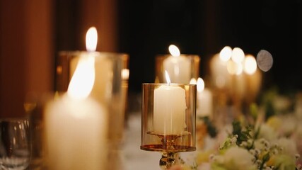 Close-up of elegant candles in glass holders glowing warmly on a decorated dinner table at night. Romantic and cozy atmosphere, perfect for weddings or special events. - Powered by Adobe