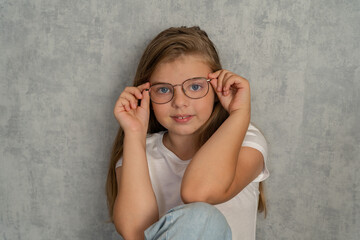 Little blonde girl wearing glasses to improve her vision and looking at the camera with...