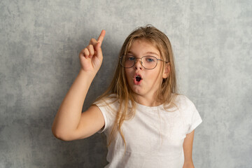 Blue-eyed girl wearing glasses to improve vision and with an inventive facial expression on a gray...