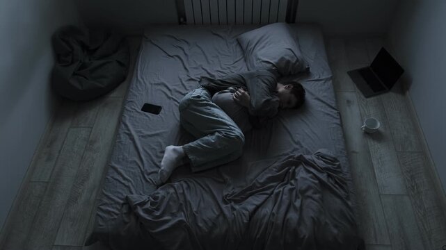 Sadness and pain after breakup. Young man hugging pillow on bed feeling lonely and heartbroken after losing his love.