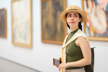 Portrait of a young Caucasian pretty woman in a straw hat and elegant clothes in the gallery of modern art. Copy space. The concept of the Museum Day