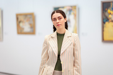 Portrait of young Caucasian woman in elegant jacket contemplating in the art gallery. Concept of cultural education and Museum Day